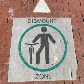 A marking on the pavement that shows a person walking their bike with the words “Dismount Zone.” 