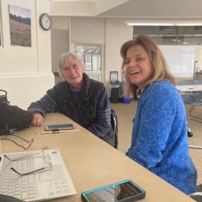 A tech coach assists an older adult with how to use a cell phone.