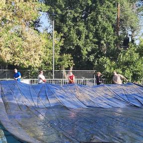 Six city staff members pulling a cover over the Spruce Street swimming pool.