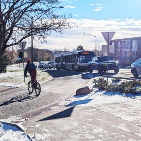 Person biking across crosswalk near Broadway while express bus and cars line up at traffic signal